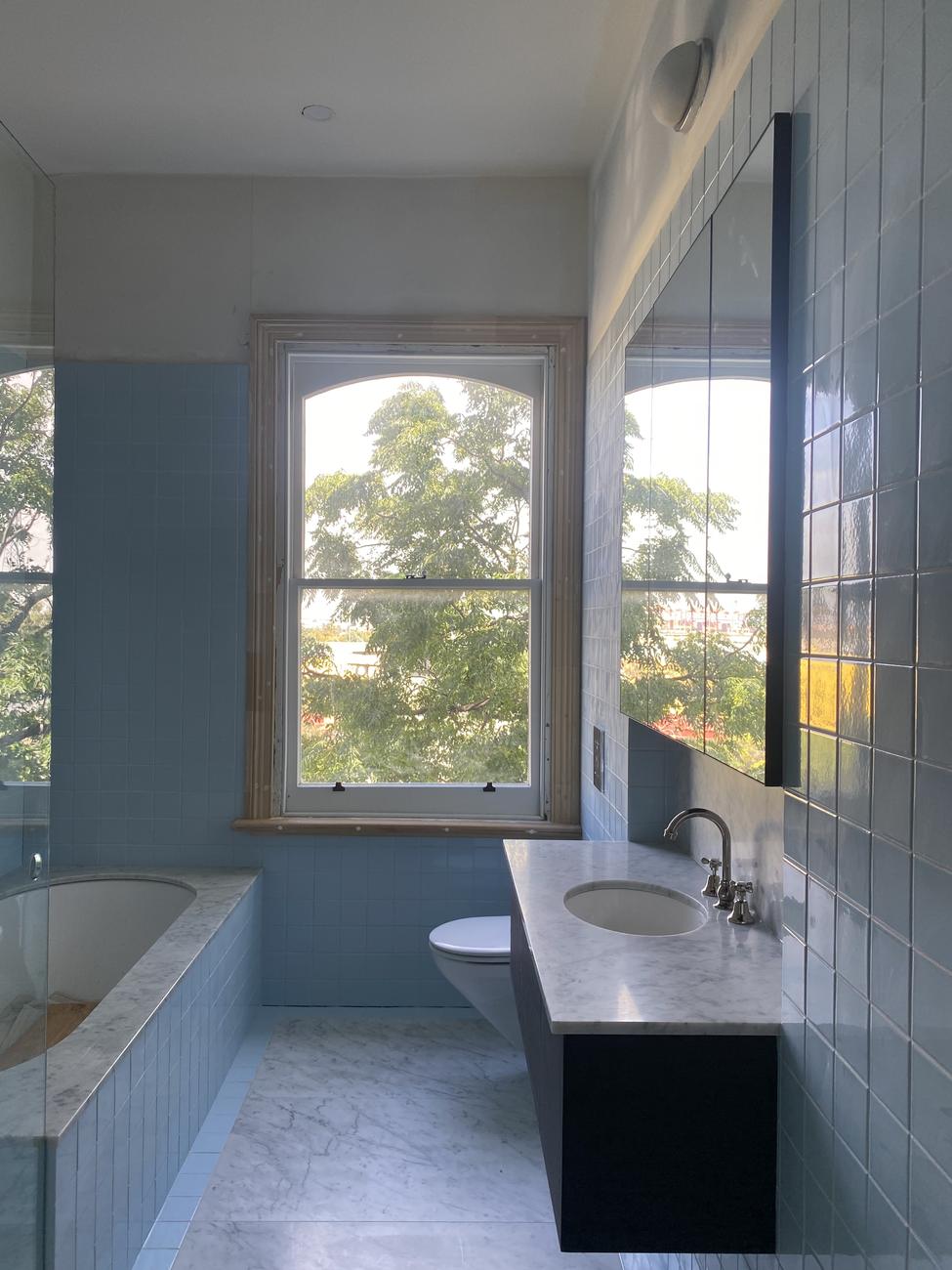 Completed bathroom renovation — blue tiling, marble benchtop and floor, timber vanity